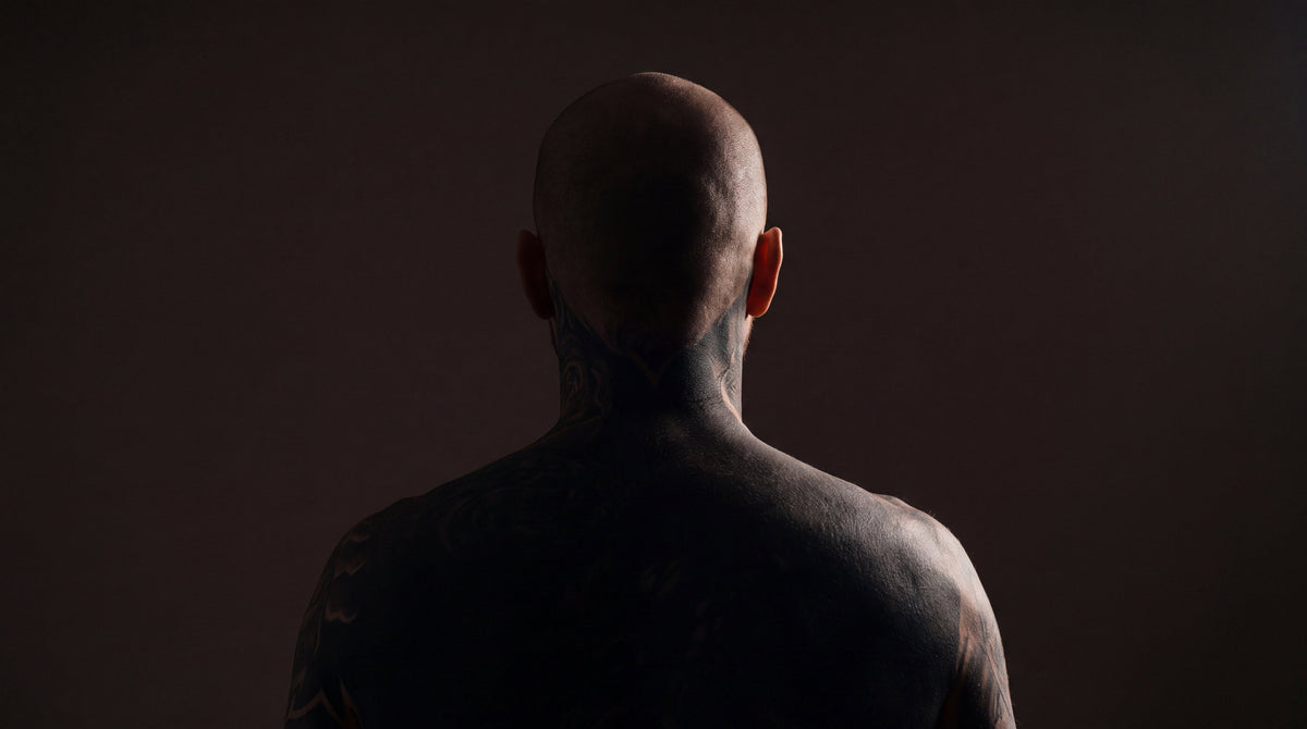 A heavily tattooed man seen from behind in near darkness, the most tattooed people on Earth