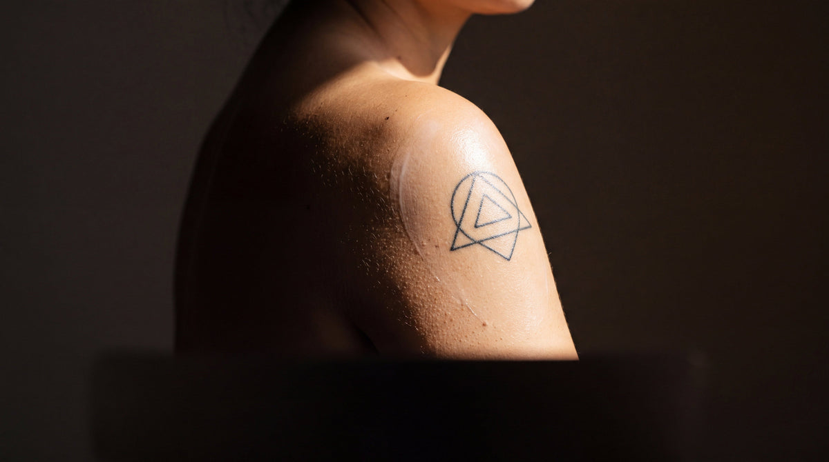 Hard sunlight crossing a fine line tattoo on a shoulder with a sheer film of lotion, protecting a tattoo from fade