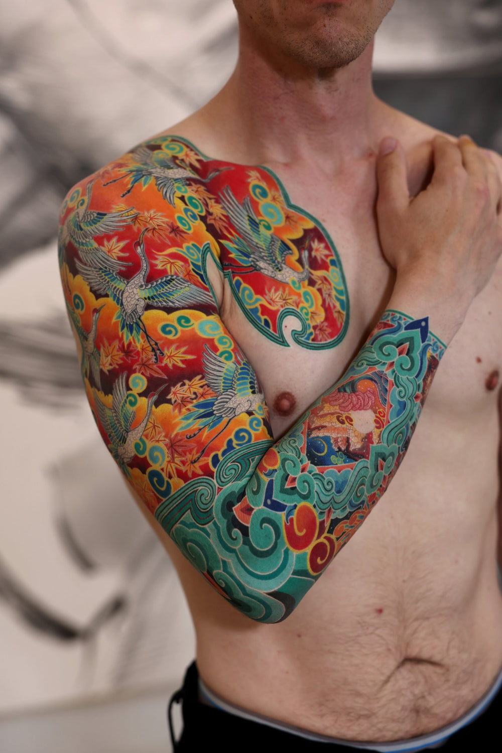 PittaKKM chest and sleeve tattoo, white cranes through gold maple and teal cloud on saturated red, with a patterned forearm