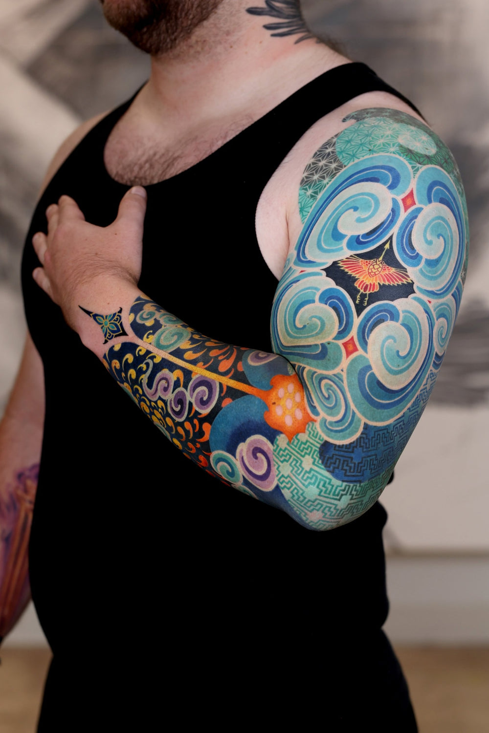 PittaKKM full sleeve tattoo of blue and white cloud spirals around a small firebird, with gold scrollwork and lotus over navy on the forearm